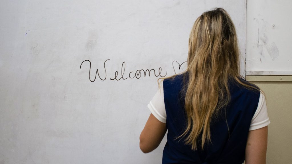 Profesora de inglés escribiendo Welcome en la pizarra durante una clase presencial.